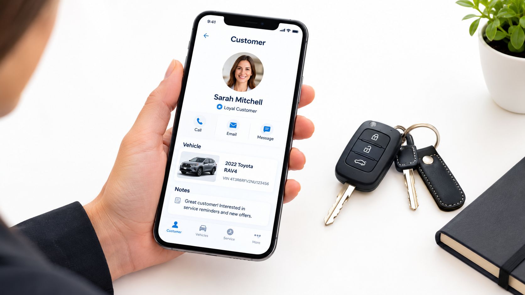A professional holding a smartphone displaying customer details for a car dealership CRM application.