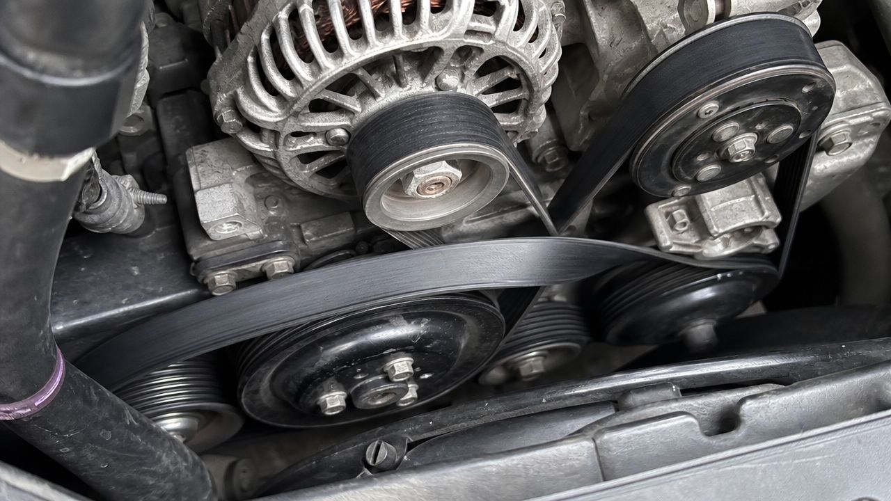 A close-up view of a car engine showing the serpentine belt threaded around the pulleys.
